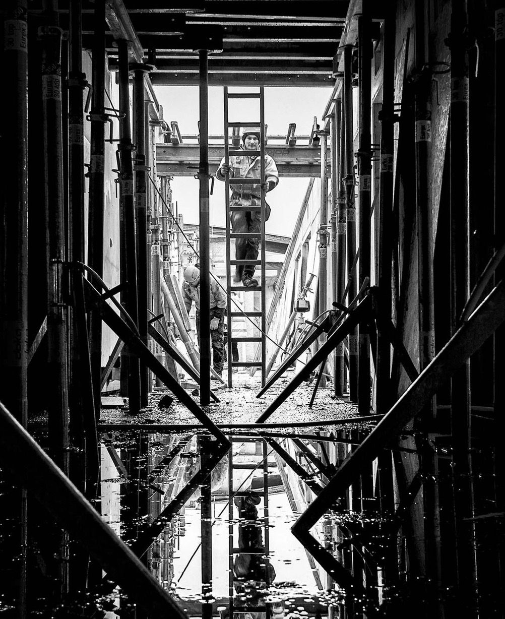 Workers on a ladder amid dark scaffolding